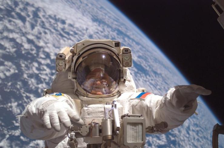 An image of an astronaut in a space suit with the earth behind him and a fellow astronaut reflected in his visor.