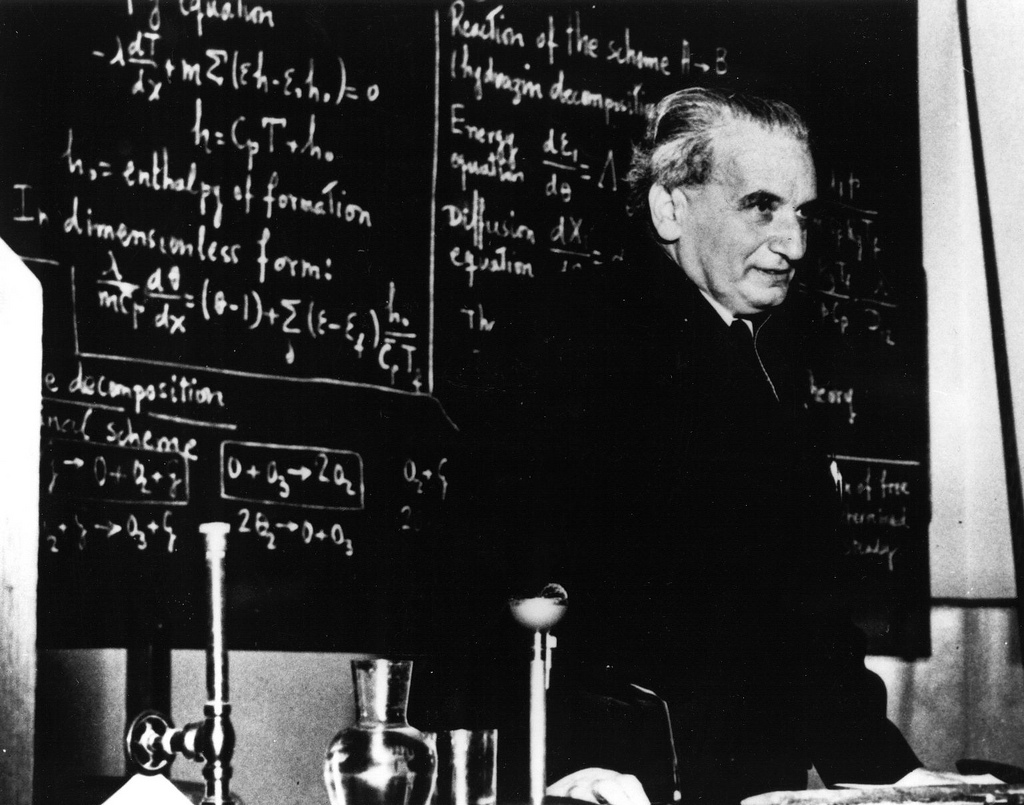 An image of Hungarian physicist Theodore von Karman in a lecture hall with a chalk board full of equations behind him.