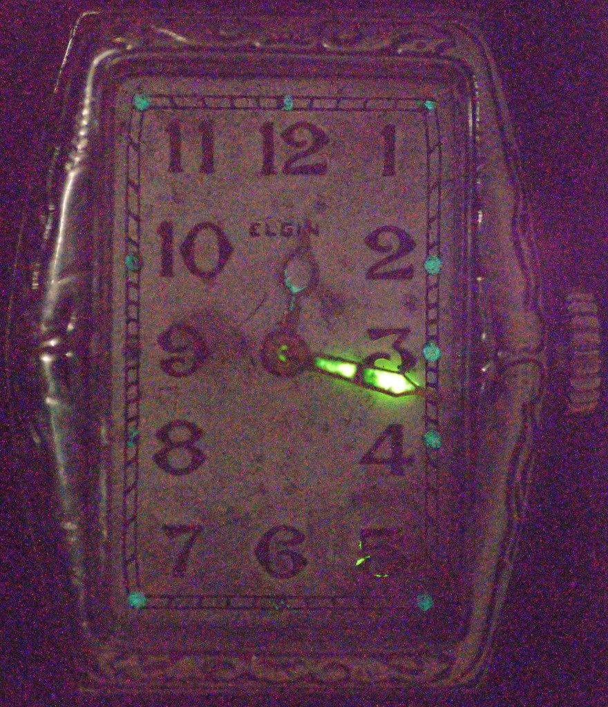 An old art deco style watch from the brand Elgin. Numbers and dials are glowing a green colour due to radium-based fluorescent paint.