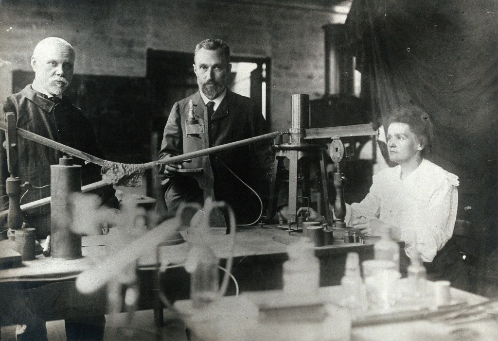 A black and white Henri Becquerel, Pierre Curie and Marie Curie in a lab surrounded by lots of lab equipment.