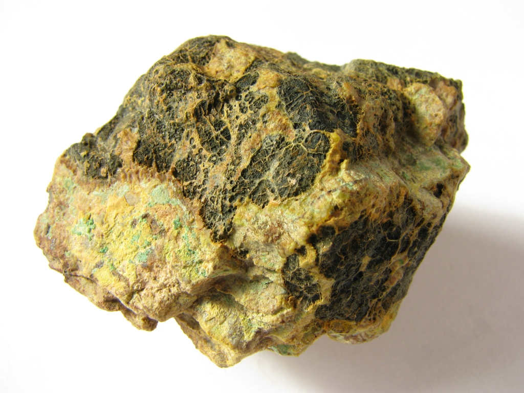 A yellow, green, and brown rock placed on a white background. Pitchblende is a rock that contains uranium ore. 